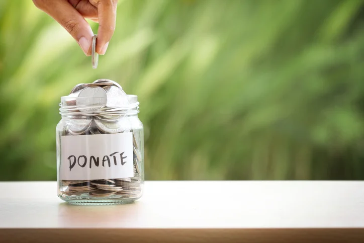 Glass jar with 'donate' sticker to front filled with silver coins