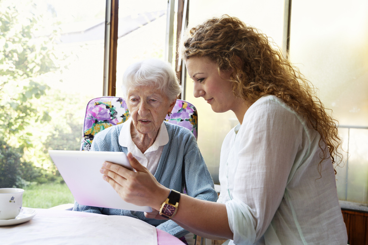 a younger lady helping an elderly lady read in conservatory