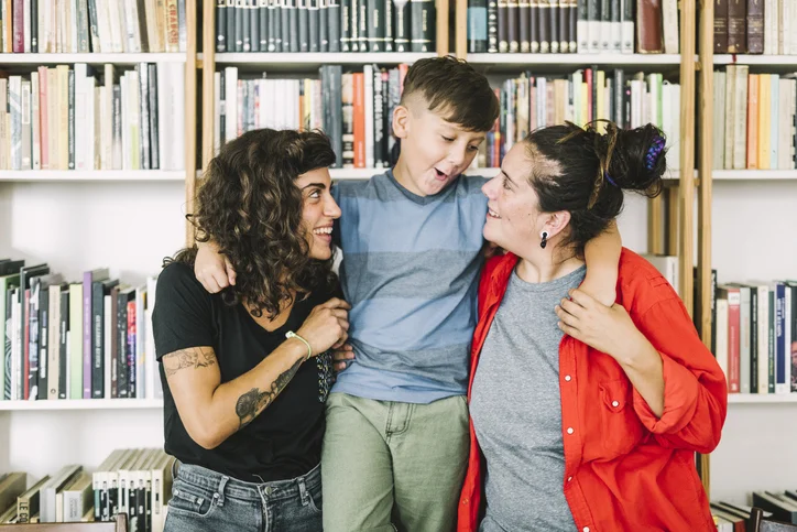 two woman and their child beside wall of books