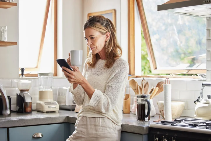 a lady leaning on the counter in a kitchen on her phone
