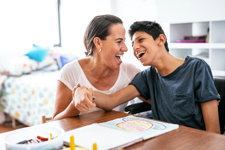 Boy with learning disability smiling and drawing with carer