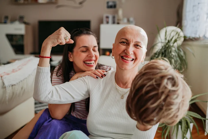 Woman with no hair holding wig and flexing with smile to face