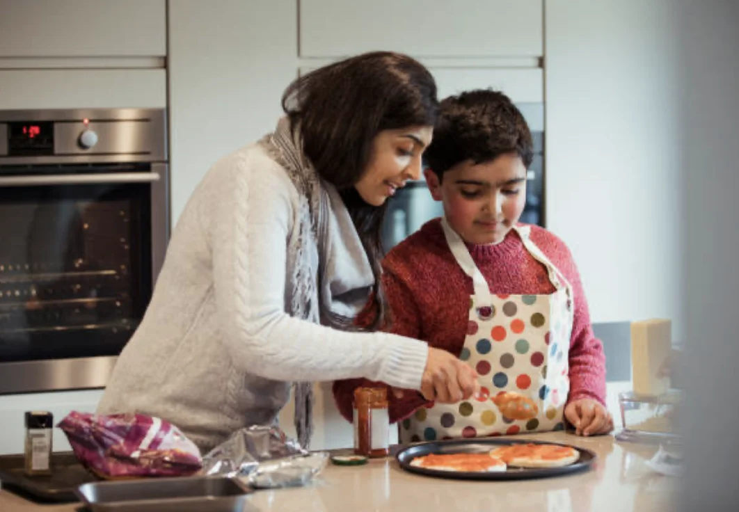 Mother and son making pizza in kitchen while wearing aprons