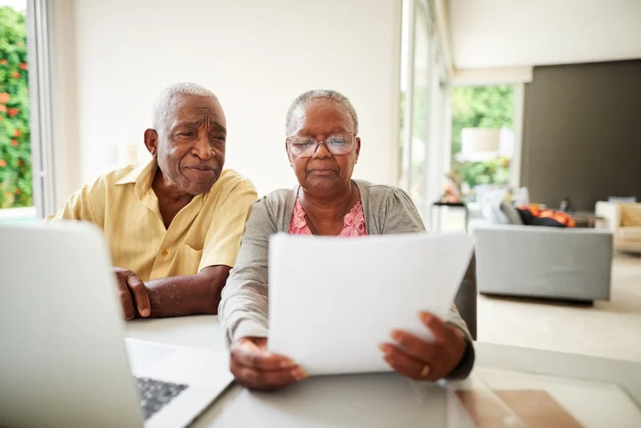 an elderly black couple reading a document beside laptop