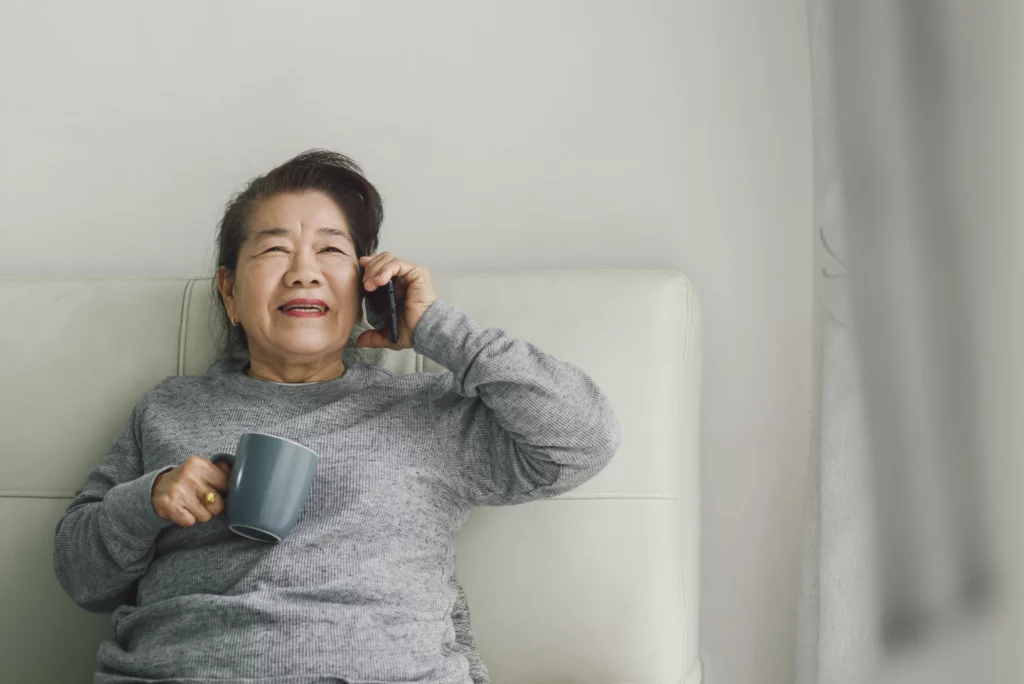 Asian senior woman talking on a phone holding a mug.