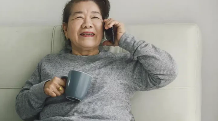 Asian woman smiling and holding a mobile phone to her ear while also holding a mug to her chest