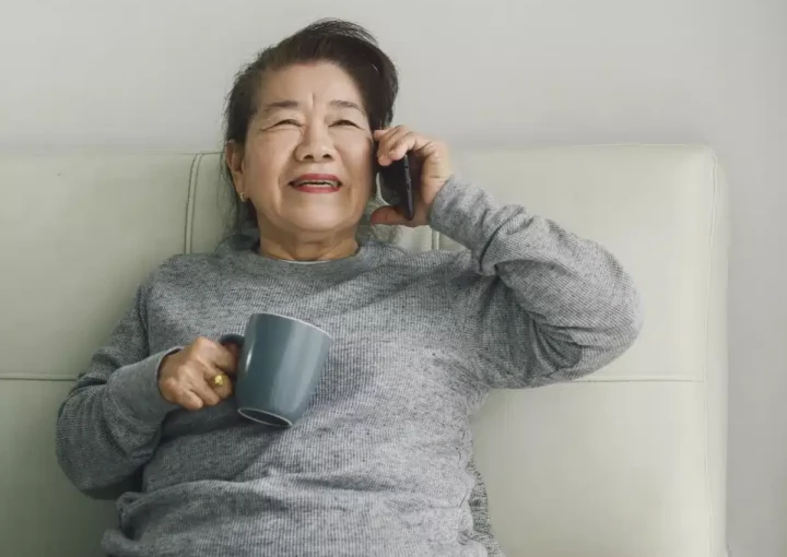 Asian woman smiling and holding a mobile phone to her ear while also holding a mug to her chest