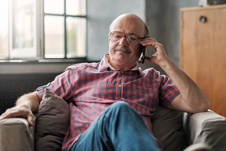 Older man who is balding and wearing glasses is speaking on the telephone