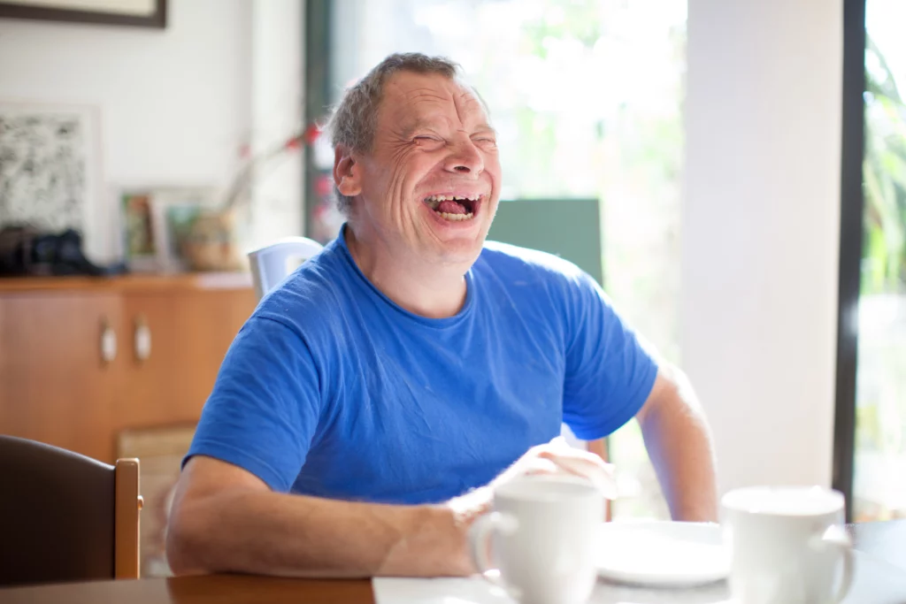 Man with learning disabilities, wearing a blue tshirt, laughing.