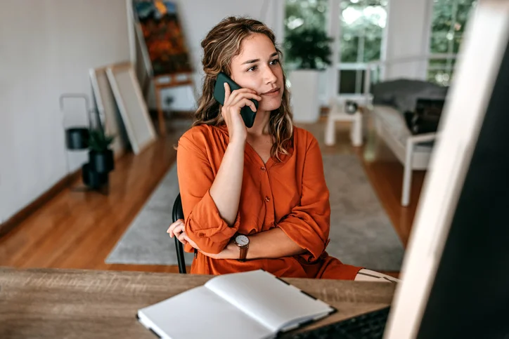 Woman in orange shirt sitting at desk with open book on phone