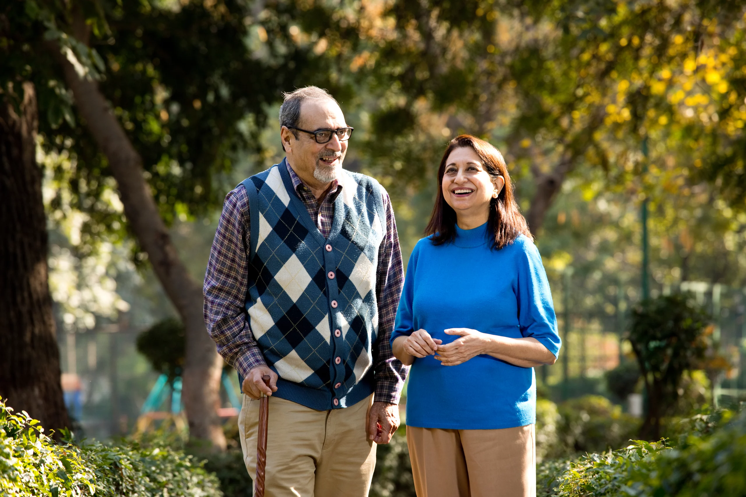 A man an a woman standing outside on a nice autumn day, smiling.