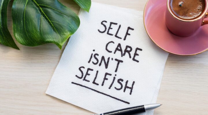 A piece of paper on the table next to a mug and leaf reads "Self care isn't selfish"