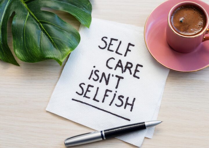 A piece of paper on the table next to a mug and leaf reads "Self care isn't selfish"