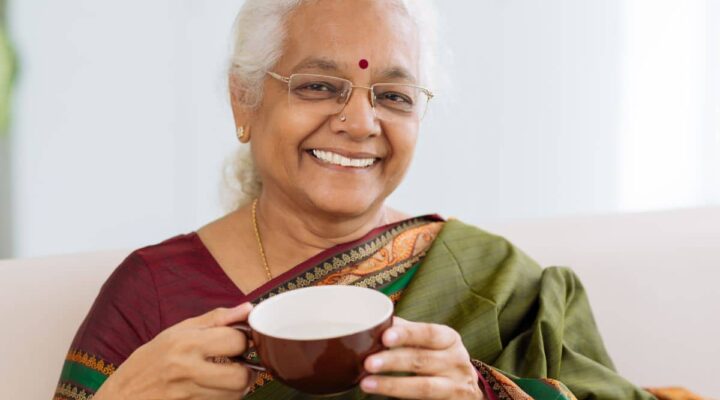 Older Indian woman smiling and holding a mug