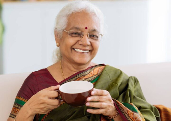 Older Indian woman smiling and holding a mug