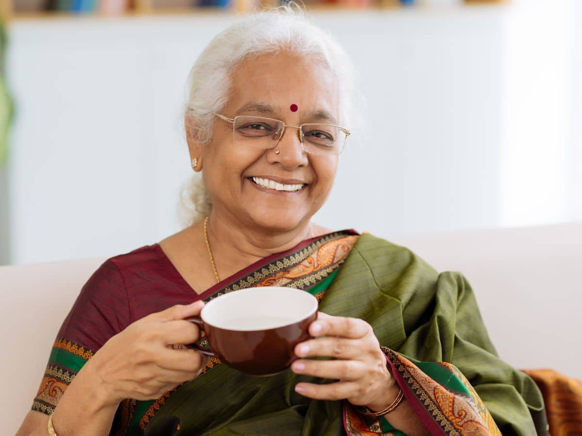 Older Indian woman smiling and holding a mug